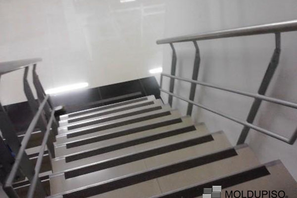 Cinta antiderrapante negra en escaleras color beige interiores de edificio con pasamanos de aluminio